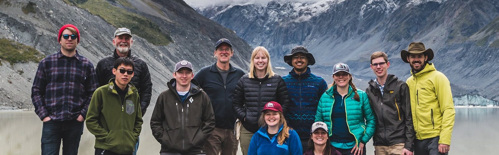 A group of Geoscience students stands in front of a river and mountains.